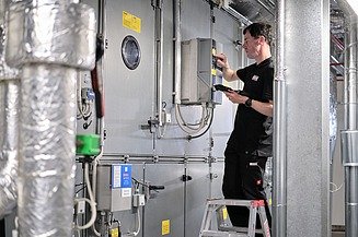 Data management Photo of an employee on a ladder at the ventilation system, transferring data to a tablet