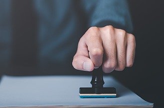 Bild von einer Hand, die eine Zertifizierung vornimmt und einen Stempel auf ein Blatt Papier drückt