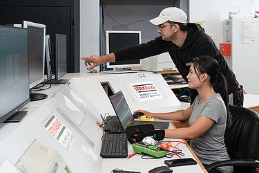 Photo of two employees at a table with monitors and a laptop top