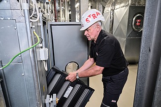 Photo of an employee in a helmet replacing the filter of a ventilation system