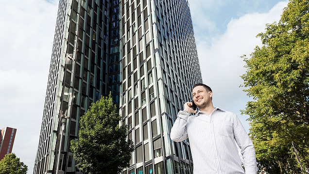 Photo of an employee standing in front of a high-rise building and talking on the phone 