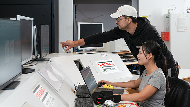 Photo of two employees at a table with monitors and a laptop top