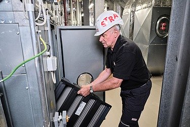 Photo of an employee in a helmet replacing the filter of a ventilation system