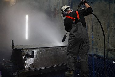 Picture of a person carrying out industrial services and cleaning a tub with a blasting process