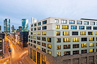 Photo of a six-story building at an intersection, with a few skyscrapers in the background