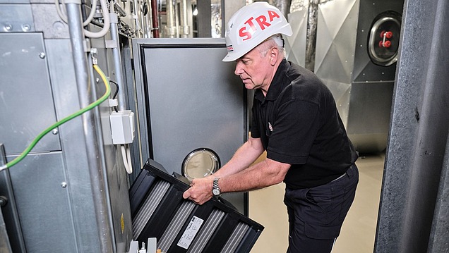 Photo of an employee in a helmet replacing the filter of a ventilation system