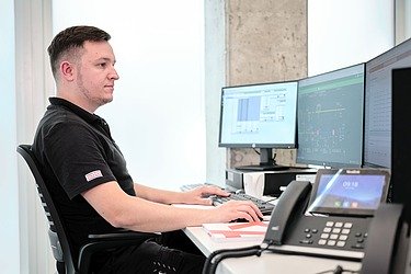 Photo of an employee at a desk with three monitors and telephone