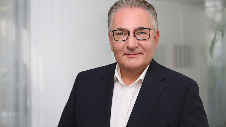 Managing Director Marko Bohm - businessman in a dark suit and striped tie smiling in front of a neutral background, professional business portrait.