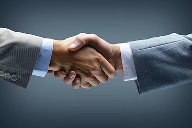 Two men in gray-blue suits and white shirts shake hands.