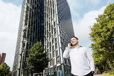 Photo of an employee standing in front of a high-rise building and talking on the phone 