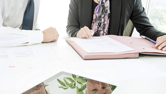 Two people checking contracts at a desk in an office, close-up of documents, hands and a tablet.