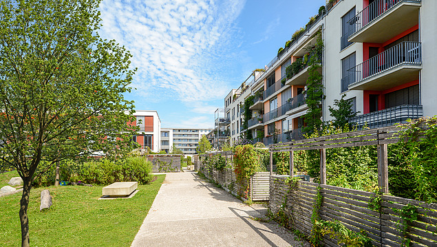 Residential complex with green areas and front gardens, blue sky.