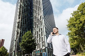 Photo of an employee standing in front of a high-rise building and talking on the phone 