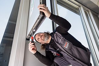 Bild von einem Mann, der Hausmeisterservices durchführt und an einem Fenster schraubt