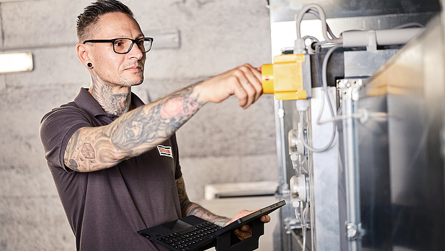 Photo of employee standing in front of a ventilation system with a tablet