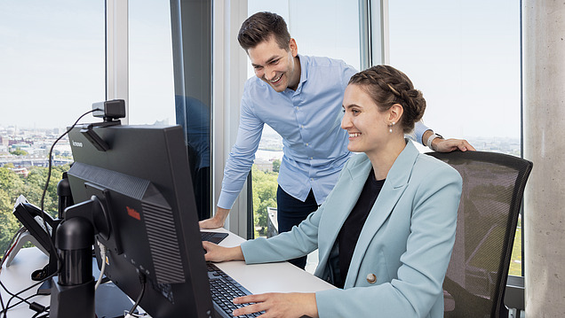 Mann und Frau sitzend an einem Tisch und haben Laptop, Tablet und zwei Mobiltelefone vor sich.