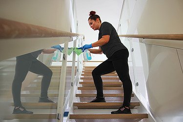 Picture of a woman cleaning a building and cleaning a railing with a cloth