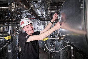 Foto von einem Mitarbeiter mit Helm, der an einer Heizungsanlage arbeitet