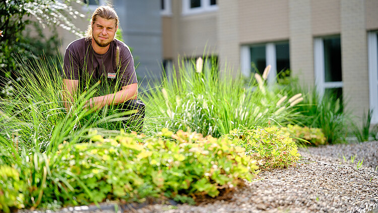 Picture of a man kneeling behind bushes by a pond