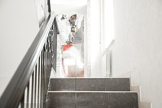 Image of a person in a protective suit carrying out pest control in a stairwell