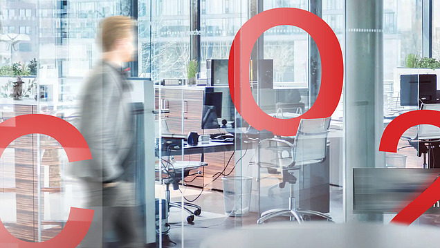 Modern office environment with glass walls, blurred person and large red CO2 lettering as a central design element.