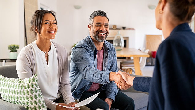 Conversation between three people, two sitting on a sofa, man and woman shaking hands.